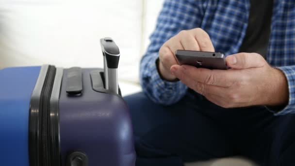 Man op reis in vakantietekst met behulp van een mobiele telefoon, persoon met smartphone in de hand wachtend in de buurt van een koffer — Stockvideo