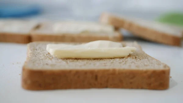 Café da manhã com manteiga no brinde, espalhando margarina em uma fatia fresca de pão na cozinha — Fotografia de Stock