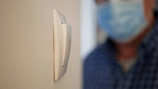 Hombre con máscara médica y guantes de protección entrar en la sala de oficina encendiendo la luz del interruptor en la pared — Foto de Stock