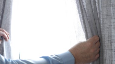 Bir adam güneşli bir sabahta otel odasında pencereyi açıyor. Bir adam pencereye bakıyor. Rahatlamış.