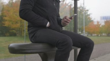 bir otobüs durağında akıllı telefon kullanan bir adam Close-Up