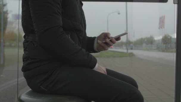 Primer plano de un hombre usando un teléfono inteligente en una parada de autobús — Vídeos de Stock