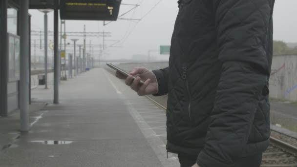 Primer plano de un hombre usando un teléfono inteligente en la estación de tren — Vídeo de stock