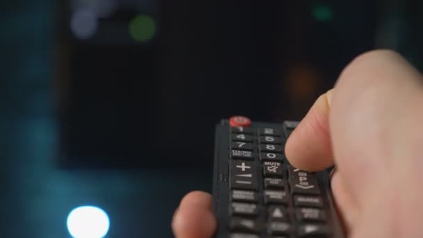 Feche a mão homem segurando o controle remoto TV e mudando de canais . — Vídeo de Stock