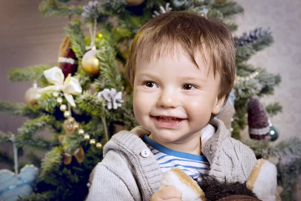 Un petit garçon joue avec un cheval à bascule autour du sapin de Noël — Photo