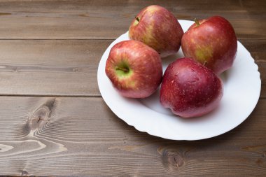 Ahşap arka plan üzerinde beyaz tabak içinde dört taze kırmızı elmalar