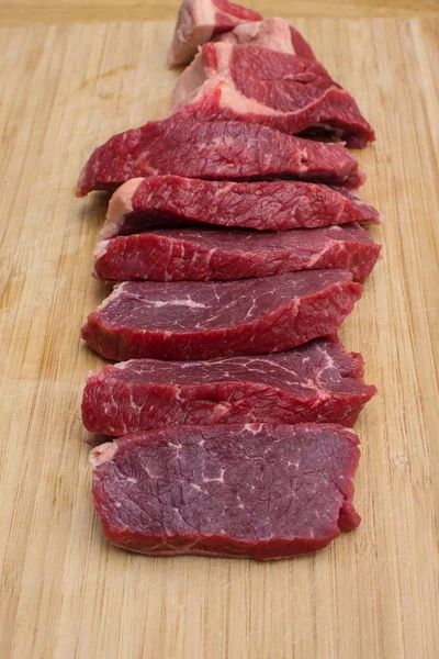 Świeże surowe mięso wołowiny w plasterki na drewnianej deski do krojenia. — Zdjęcie stockowe