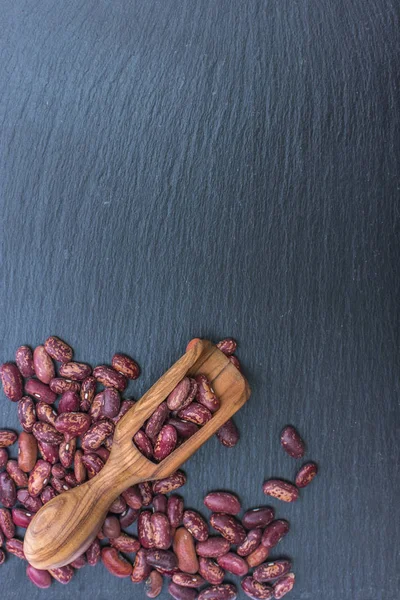 Feijão vermelho orgânico e colher de madeira de oliveira em fundo preto de ardósia ou pedra — Fotografia de Stock