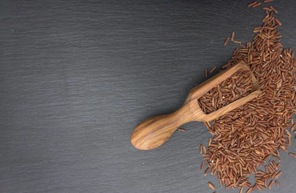 Czerwony ryż i oliwnymi drewna scoop na czarnym tle z łupków lub kamienia. — Zdjęcie stockowe