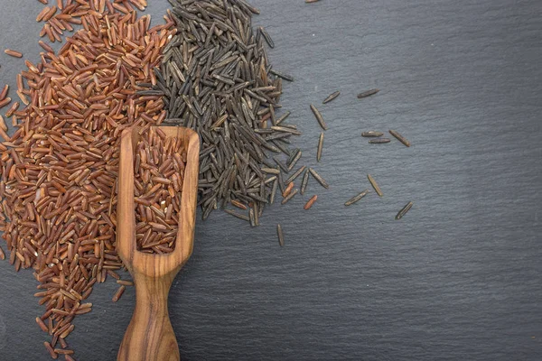 Scoop di riso rosso e legno d'ulivo su fondo nero di ardesia o pietra . — Foto Stock