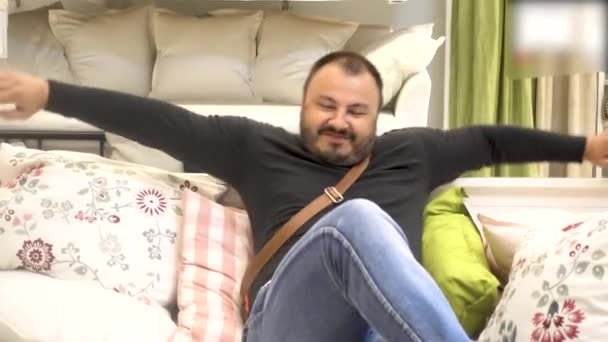 Ευτυχισμένος χαμογελαστός άνθρωπος με ένα χαλαρωτικό γενειάδα και χαμογελαστός κάθεται στον καναπέ — Αρχείο Βίντεο