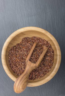 Kırmızı pirinç ve kayrak veya taş siyah arka plan üzerine ahşap bir kasede zeytin ahşap Kepçe