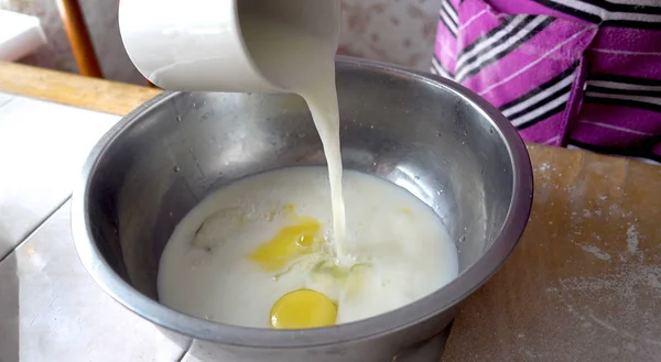 Preparation for kneading the dough. The basis of the dough. Pouring milk into a metal bowl with eggs — Stock Photo, Image