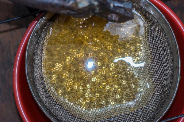 Strain the poured honey through a sieve. Filtering raw honey. Honey pouring through a sieve from honey extractor — Stock Photo, Image