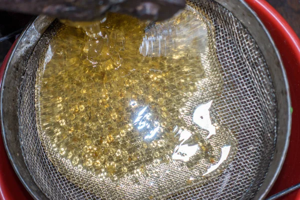 Strain the poured honey through a sieve. Filtering raw honey. Honey pouring through a sieve from honey extractor — Stock Photo, Image