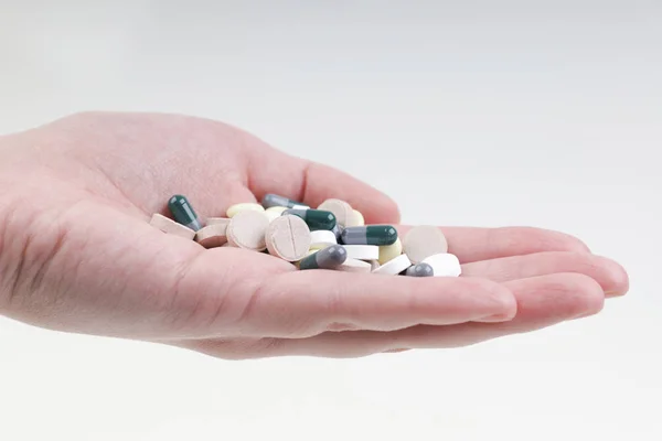 Bir adam avucunun içinde çok renkli haplar ve kapsüller tutar. 