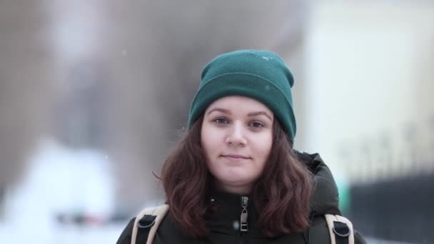 Una giovane donna è in piedi sotto la nevicata e guarda la fotocamera . — Video Stock