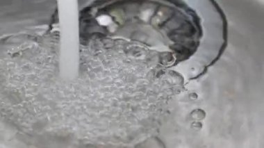 Musluktan su dolu bir lavaboya akar. Suda hava kabarcıkları. Ağır çekimde.