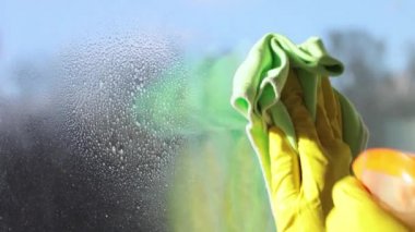 Sarı eldivenli bir adam pencereyi temizler. Pencere temizleyicisini kirli bir pencereye sıkıyor. Güneşli bir gün.