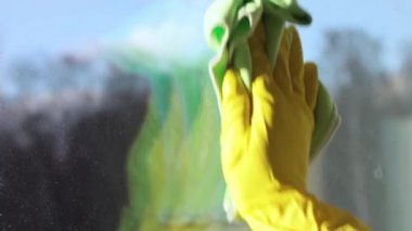 Sarı eldivenli bir adam pencereyi temizler. Pencere temizleyicisini kirli bir pencereye sıkıyor. Güneşli bir gün.