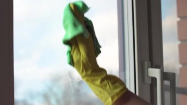 Sarı eldivenli bir adam pencereyi temizler. Pencere temizleyicisini kirli bir pencereye püskürtür.