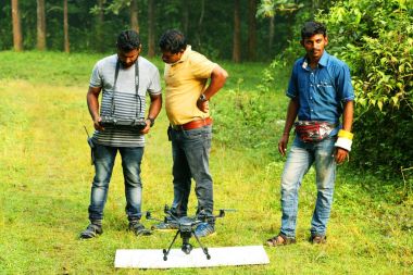 Kodaikanal, Hindistan - 21 Haziran 2016: İki yardımlı fotoğrafçı ile genç adam radyo kontrollü quadcopter ile video çekim, genç erkek uzaktan kamera yaz gezisi sırasında uçan üzerinde fotoğraf çekme.