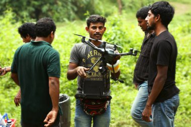 Kodaikanal, Hindistan - 21 Haziran 2016: İki yardımlı fotoğrafçı ile genç adam radyo kontrollü quadcopter ile video çekiyor,