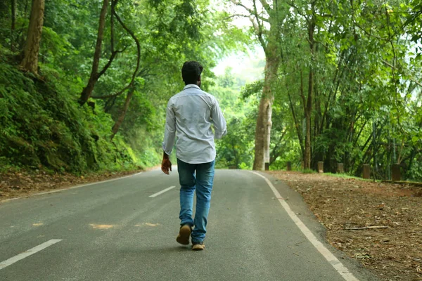 Un retrato de un hombre del sur de Asia caminando por la carretera vacía en el bosque —  Fotos de Stock