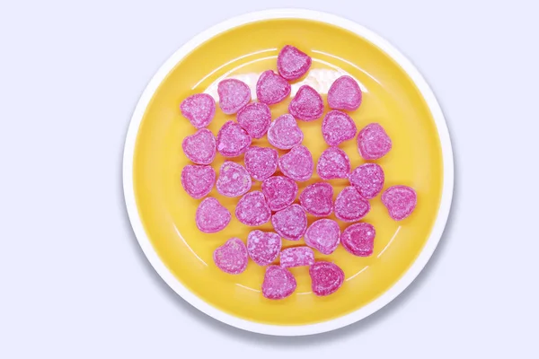 Dulces de colores brillantes en un plato amarillo sobre una vista superior de fondo blanco — Foto de Stock