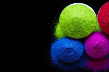 Koyu arkaplanda izole edilmiş kâselerdeki renkli holi tozunun üst görünümü.