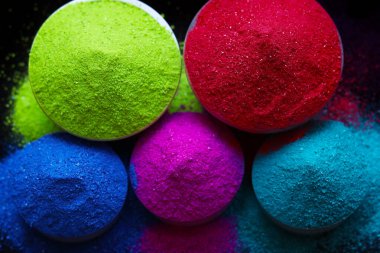 Koyu arkaplanda izole edilmiş kâselerdeki renkli holi tozunun üst görüntüsü