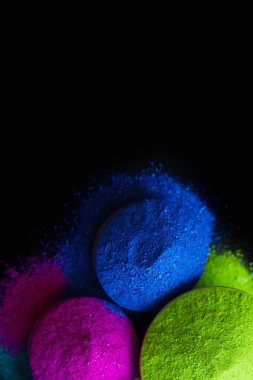 Koyu arkaplanda izole edilmiş kâselerdeki renkli holi tozunun üst görünümü.