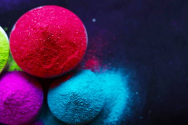 Koyu arkaplanda izole edilmiş kâselerdeki renkli holi tozunun üst görüntüsü. Metin için boşluk.