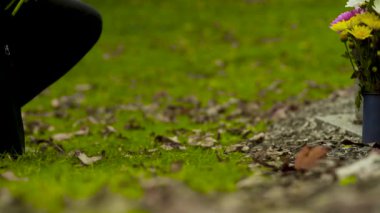 Yakından bir buket güzel çiçeği mezar taşına koyar.