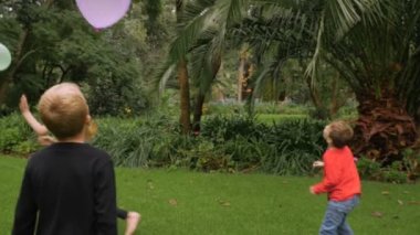 Üç küçük çocuklar eğleniyor balonları bir parkta - slomo isabet