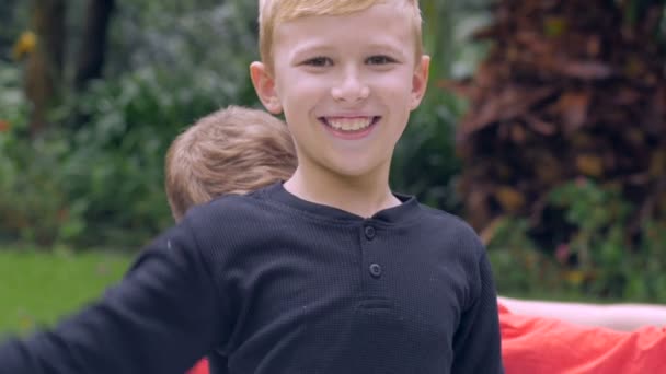 Egy aranyos mosolygós fiatal szőke fiú lemond karja mások háta mögött hullámzó — Stock videók
