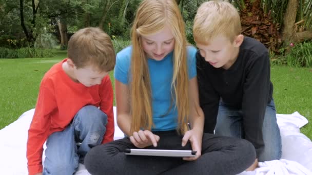 Three young children play together on a single tablet outside - slowmo handheld — ストック動画