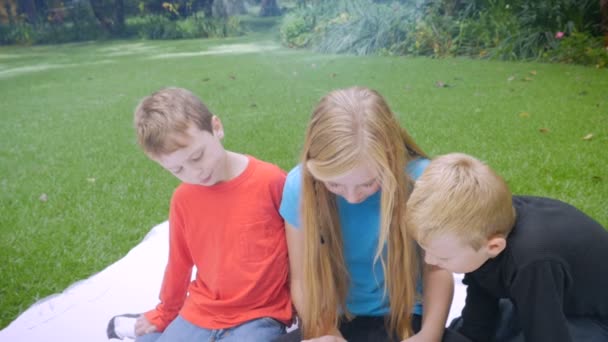 3 young kids play on a tablet outside - slowmo crane shoot — Stock video