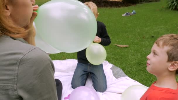 Ein kleiner Junge blickt in die Kamera, als seine Mutter seinen Ballon in die Luft sprengt - — Stockvideo