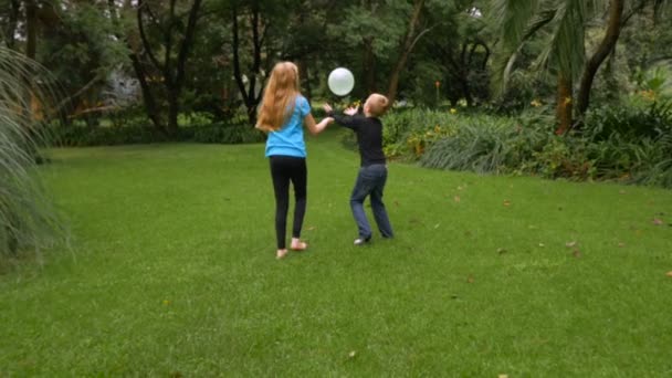 Two young children having fun hitting balloons in the air at a park - slomo Wide — Stock Video