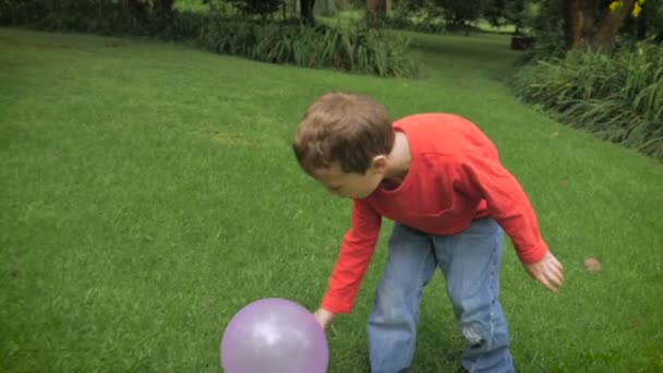 Un jeune garçon en chemise rouge aux cheveux roux joue dehors avec un ballon - slowmo 