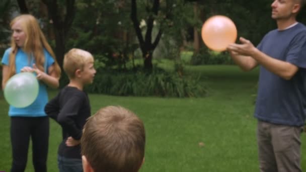 Un grupo de niños juega con su padre en un parque con globos - slow mo — Vídeos de Stock