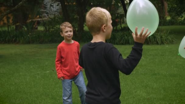 Three happy young children play a game in a park with balloons - slowmo handheld — Stock video