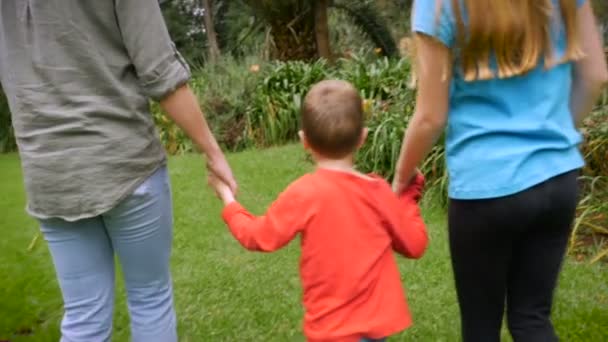 Een moeder en haar twee kinderen houdt handen terwijl ze door een park lopen — Stockvideo