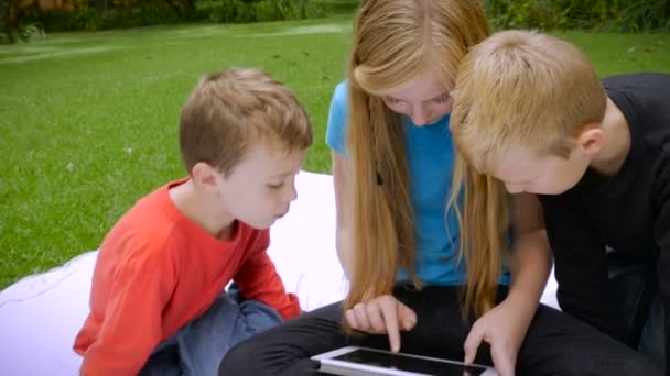 Una hermana le muestra a sus dos hermanos más jóvenes algo en una tableta - cámara de mano lenta — Vídeo de stock