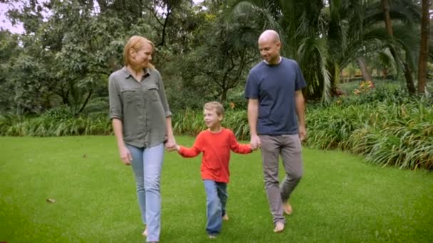 Eltern halten die Hände ihres Sohnes und drehen ihn beim Spazierengehen im Park um — Stockvideo
