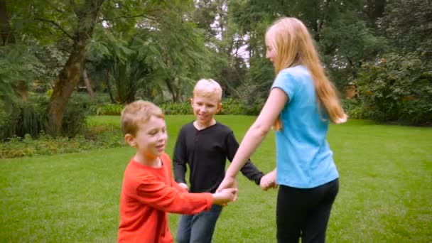 Троє маленьких дітей грають кільце навколо троянди в парку в повільному темпі — стокове відео