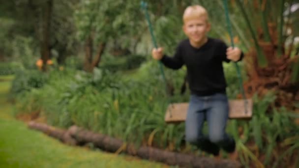 Un niño rubio feliz divirtiéndose balanceándose en un viejo columpio de árbol de moda - slow mo — Vídeo de stock