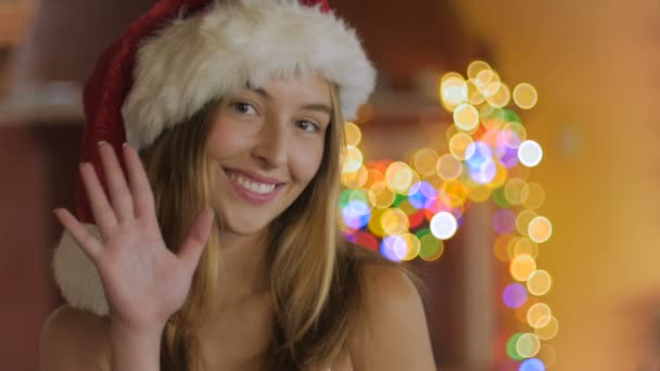 Eine freundliche, schöne, blonde junge Frau verzichtet in die Kamera und trägt einen Weihnachtsmannhut — Stockvideo