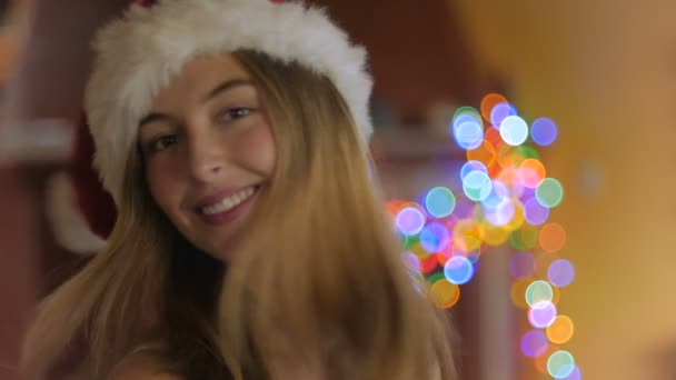 Een mooie jonge vrouw draait en kijkt naar de camera dragen een kerstmuts — Stockvideo